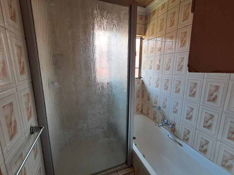 A dated bathroom featuring a combined bathtub and shower enclosure with patterned wall tiles and chrome fixtures.