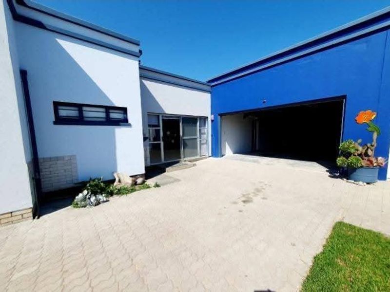 Front exterior view featuring a paved driveway, double garage entrance, and modern white and blue facade with sliding glass door access.