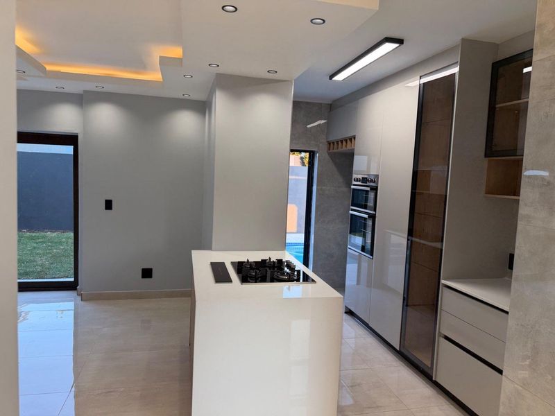 Modern, high-end kitchen featuring a central island with a gas hob, built-in ovens, sleek cabinetry, and recessed lighting, opening directly to the garden.