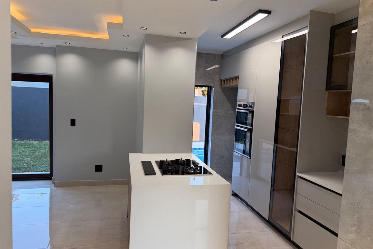 Modern, high-end kitchen featuring a central island with a gas hob, built-in ovens, sleek cabinetry, and recessed lighting, opening directly to the garden.