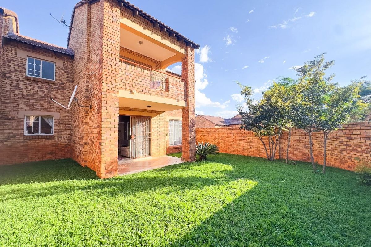 Rear view of a face brick townhouse featuring a private garden, covered patio, and an upper-level balcony.