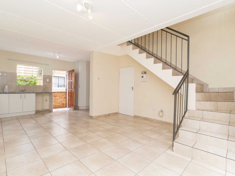Open-plan living area featuring tiled flooring, a staircase with metal railing, and a functional kitchen with built-in cabinetry and appliances.