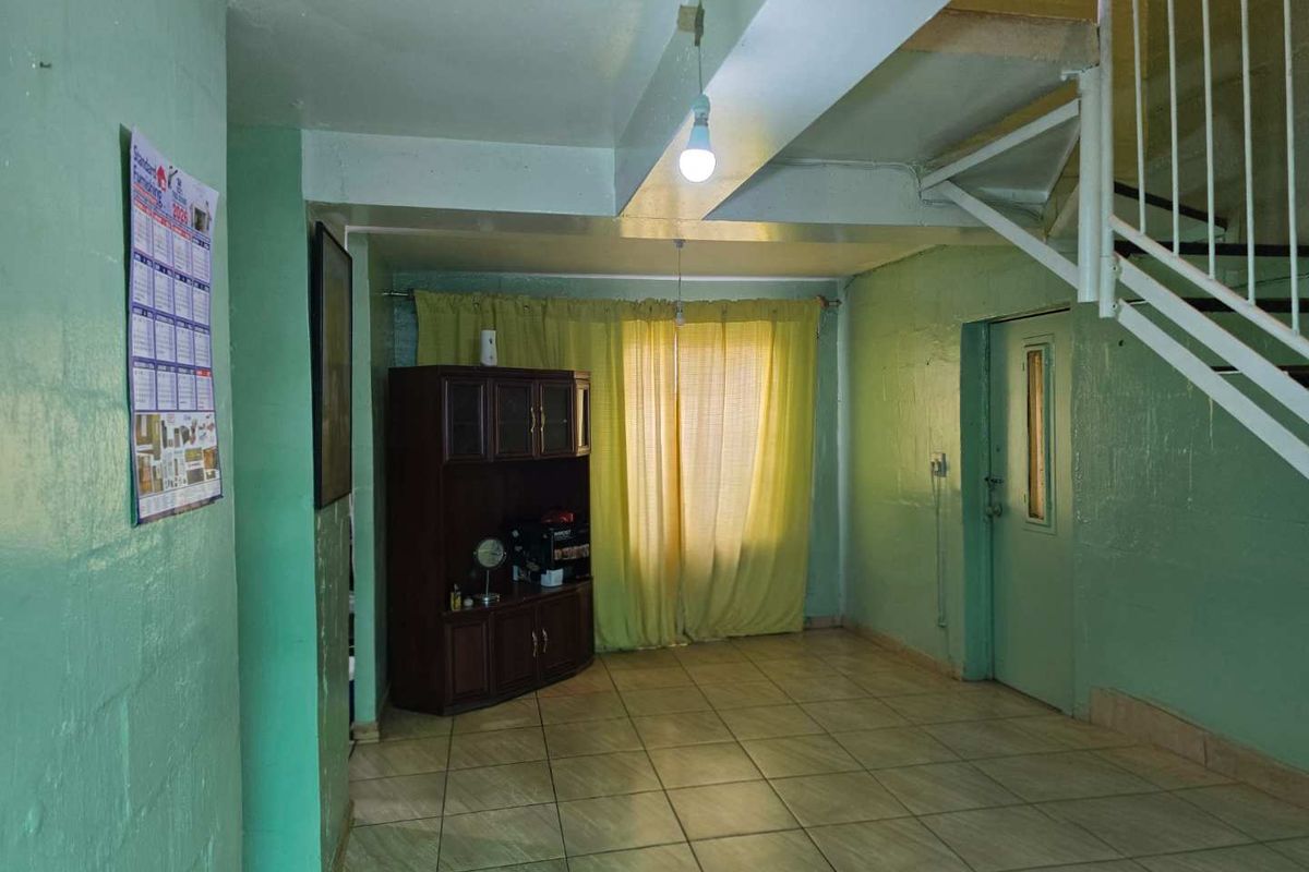 A living area featuring tiled flooring, exposed ceiling beams, and a staircase with a metal railing, providing a functional base for renovation.