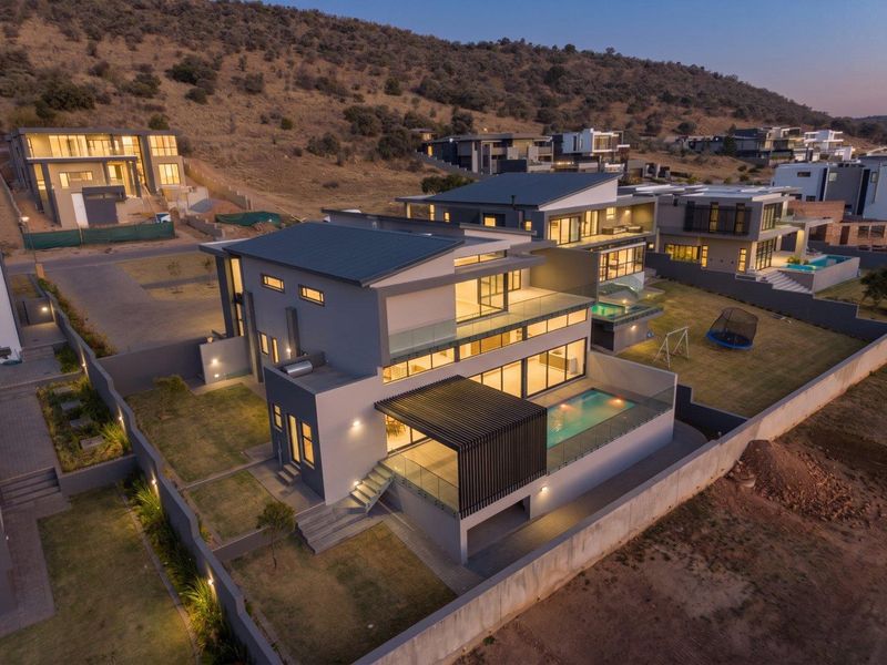 Aerial view of a modern multi-story residential property featuring a swimming pool, glass balustrades, and a covered patio area at dusk.