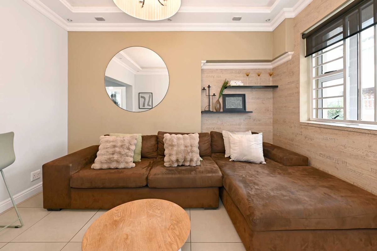 A well-maintained living room featuring recessed ceiling lighting, decorative crown molding, built-in wall shelving, and large format floor tiles.
