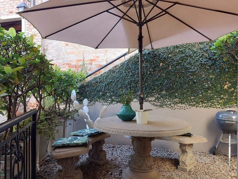A private outdoor patio area featuring gravel flooring, a retaining wall with climbing greenery, and metal safety railings.