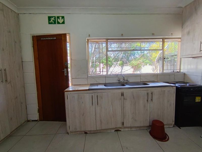 A functional kitchen featuring built-in cabinetry, a double sink, and tiled flooring, with a window providing natural light and garden views.