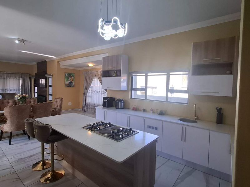 Spacious open-plan living and kitchen area featuring a modern kitchen island with gas hob, sleek cabinetry, and polished tiled flooring throughout.