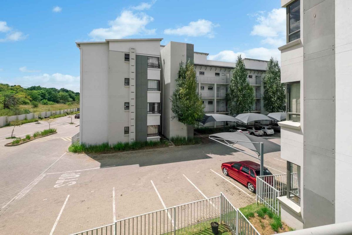 View of the apartment complex exterior, featuring paved parking areas with shade-cloth carports and surrounding landscaped grounds.