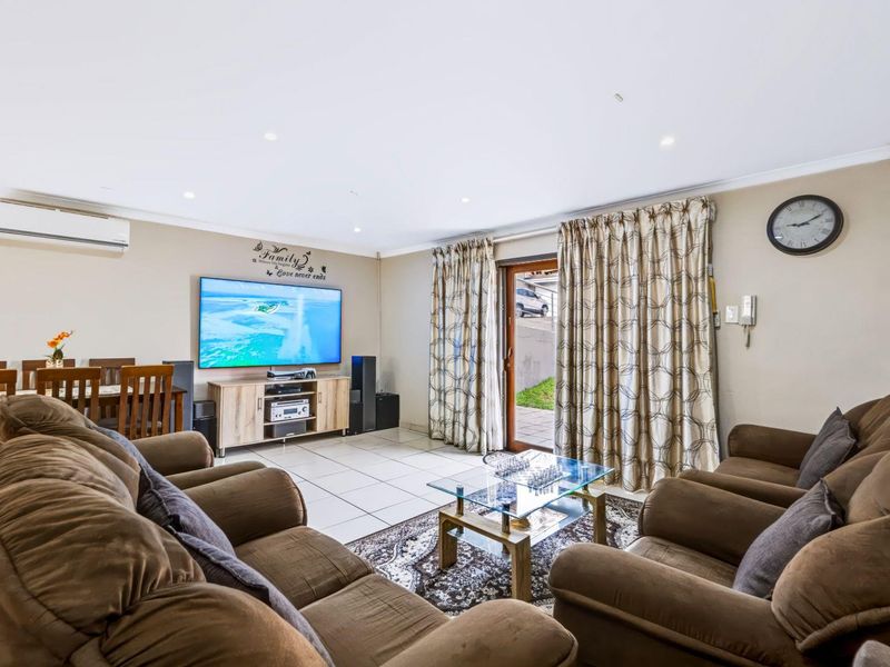 A well-maintained living room featuring tiled flooring, recessed lighting, and a split-system air conditioner, with direct access to the outdoor area via a sliding door.