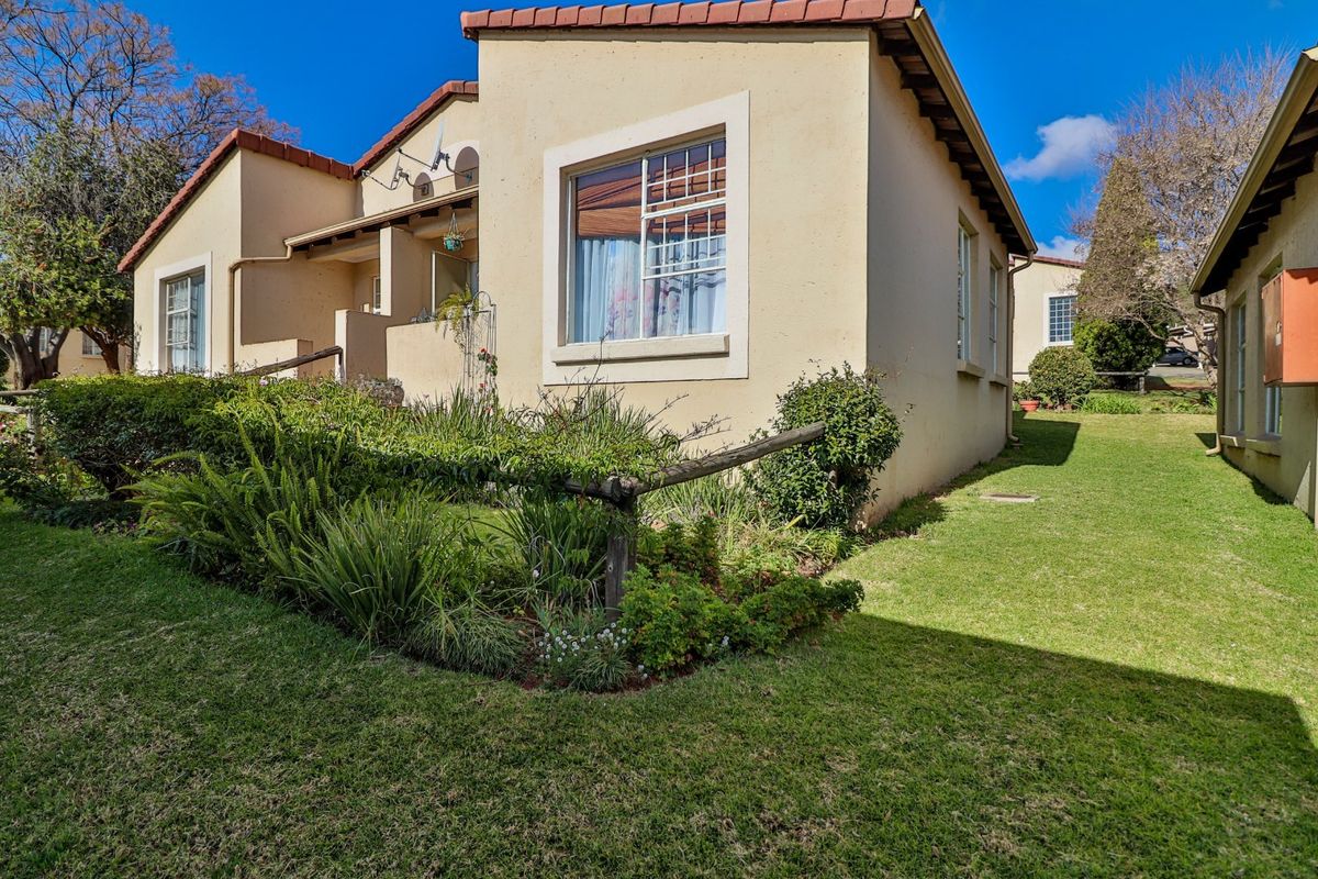 A view of the rear exterior of the townhouse, featuring plastered walls, a tiled roof, and a well-maintained garden area.