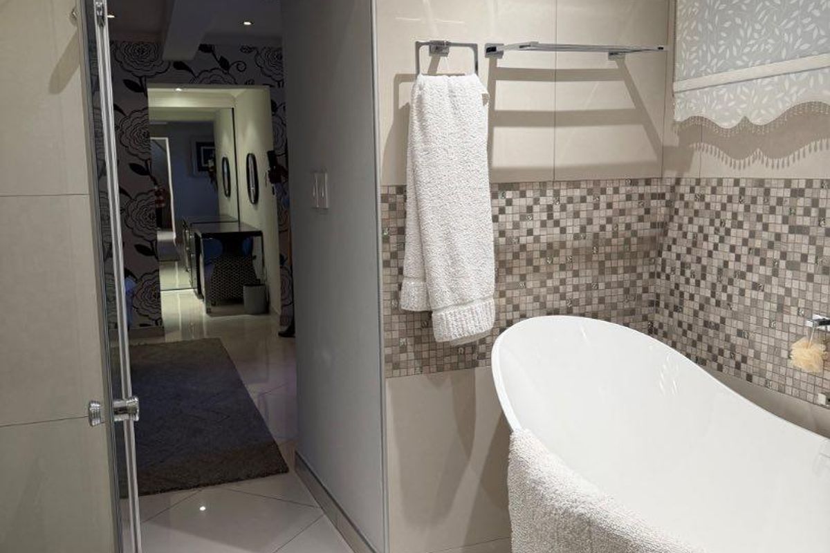 Modern bathroom featuring a freestanding bathtub, glass shower enclosure, and neutral tiled finishes with decorative mosaic accents.