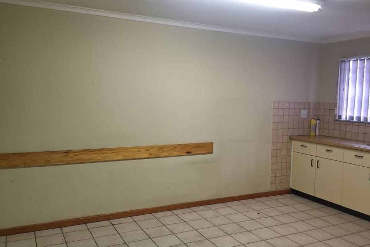 An empty industrial kitchen space featuring tiled flooring, built-in cabinetry with a tiled splashback, and functional fluorescent lighting.