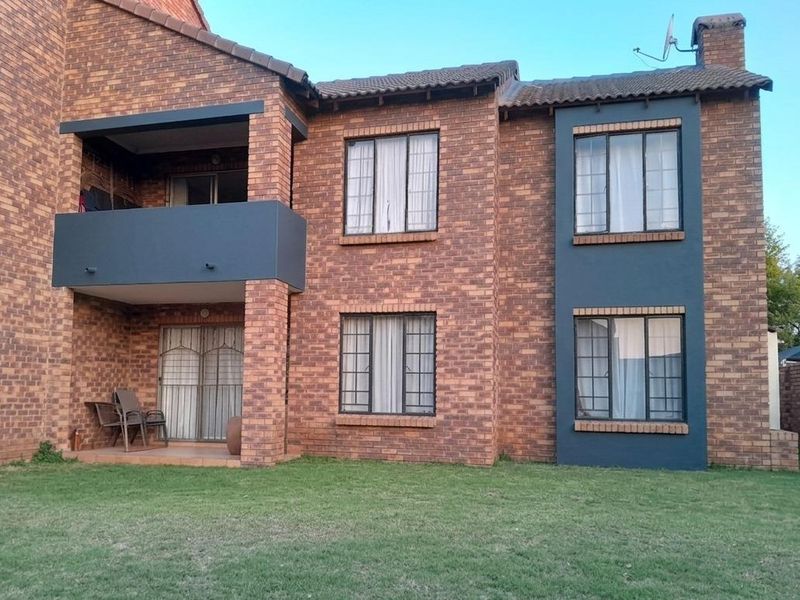 Rear view of a two-story face brick apartment building featuring a ground floor patio, an upper-level balcony, and a shared garden area.