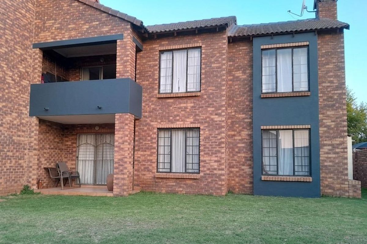 Rear view of a two-story face brick apartment building featuring a ground floor patio, an upper-level balcony, and a shared garden area.