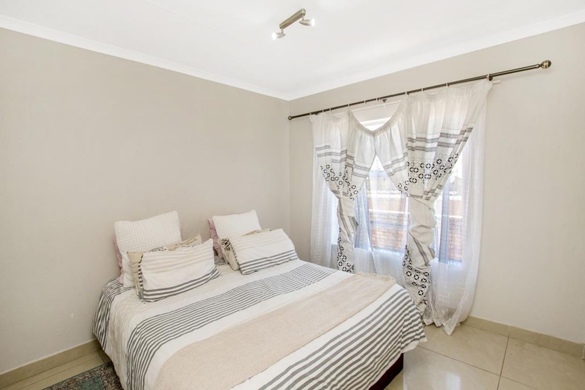A well-lit bedroom featuring neutral wall tones, tiled flooring, and a window with curtain rod fixtures.