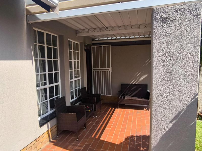 A covered patio area featuring terracotta tile flooring, security gate access, and lattice windows, providing a functional outdoor space for relaxation.