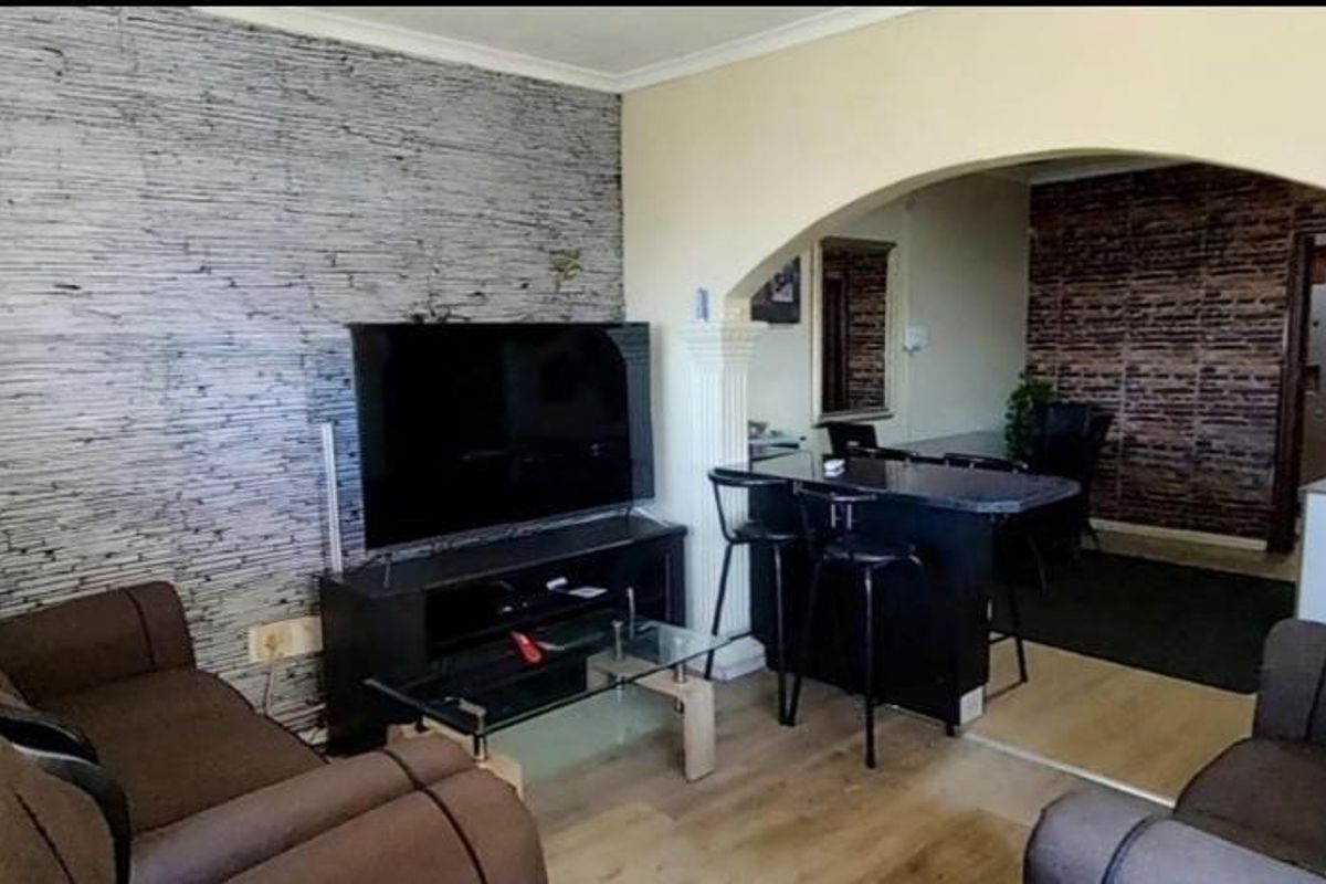 Living room featuring an arched entryway with decorative columns, laminate flooring, and a textured feature wall, leading into an adjacent dining or kitchen area.
