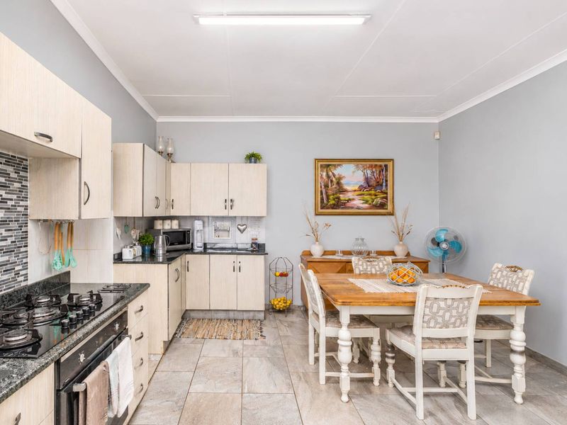 Open-plan kitchen and dining area featuring light wood cabinetry, granite countertops, gas hob, built-in oven, and neutral tiled flooring.