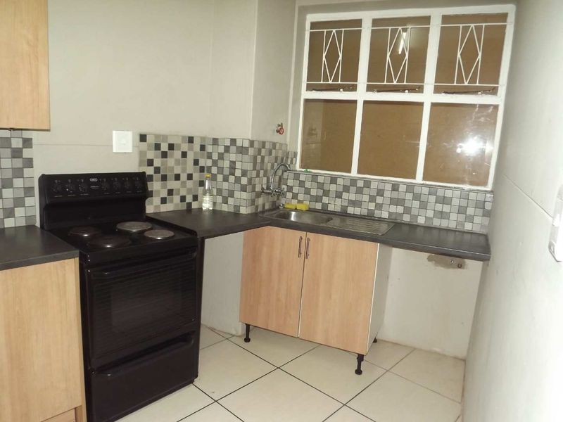 Compact kitchen featuring light wood-finish cabinetry, mosaic tile backsplash, dark countertops, and a functional freestanding stove with security-barred window.