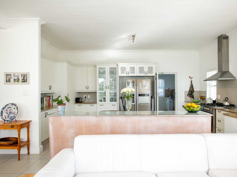 Bright open-plan kitchen featuring white cabinetry, a central island, stainless steel appliances, and tiled flooring, seamlessly connecting to the living area.
