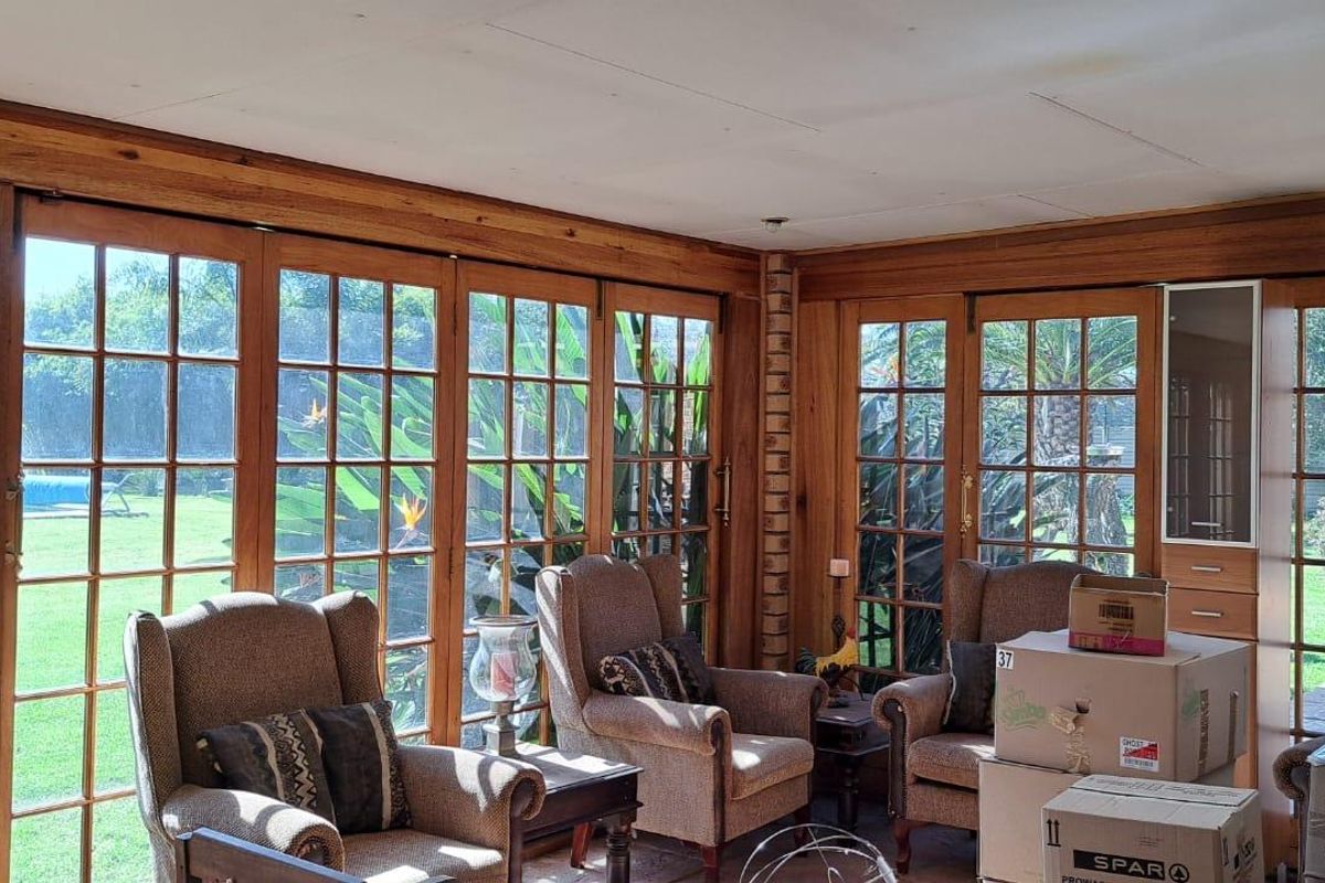 A sunroom featuring extensive timber-framed glass doors and windows, offering views of the garden and brick feature wall detailing.