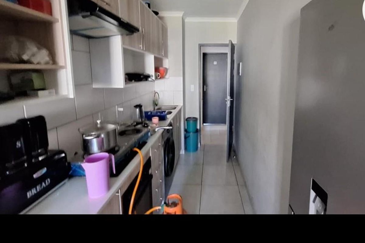 A functional galley-style kitchen featuring built-in cabinetry, a gas hob with extractor fan, and tiled flooring, leading towards an interior hallway.