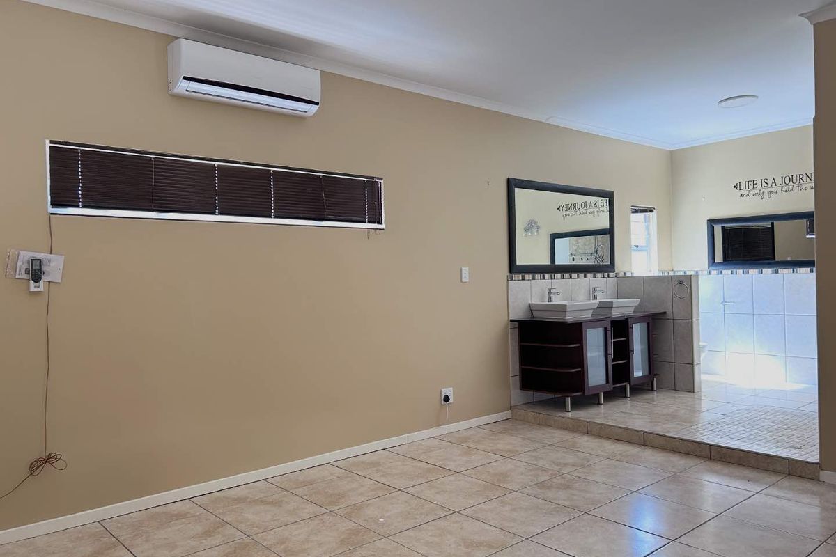 Open plan bedroom area featuring a raised en-suite bathroom section with dual vanity basins, tiled flooring, and a wall-mounted air conditioning unit.