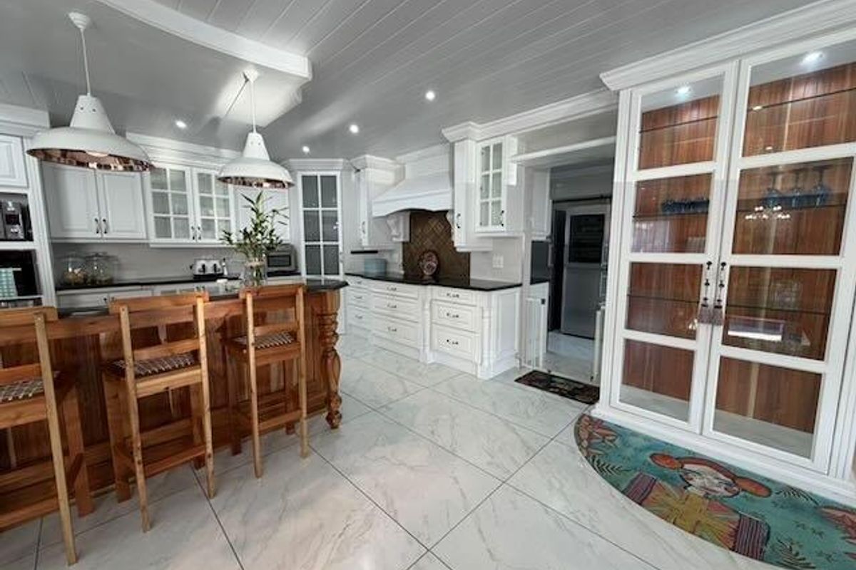 A well-appointed kitchen featuring white cabinetry, a central island with breakfast bar seating, integrated display cabinets, and modern tiled flooring.