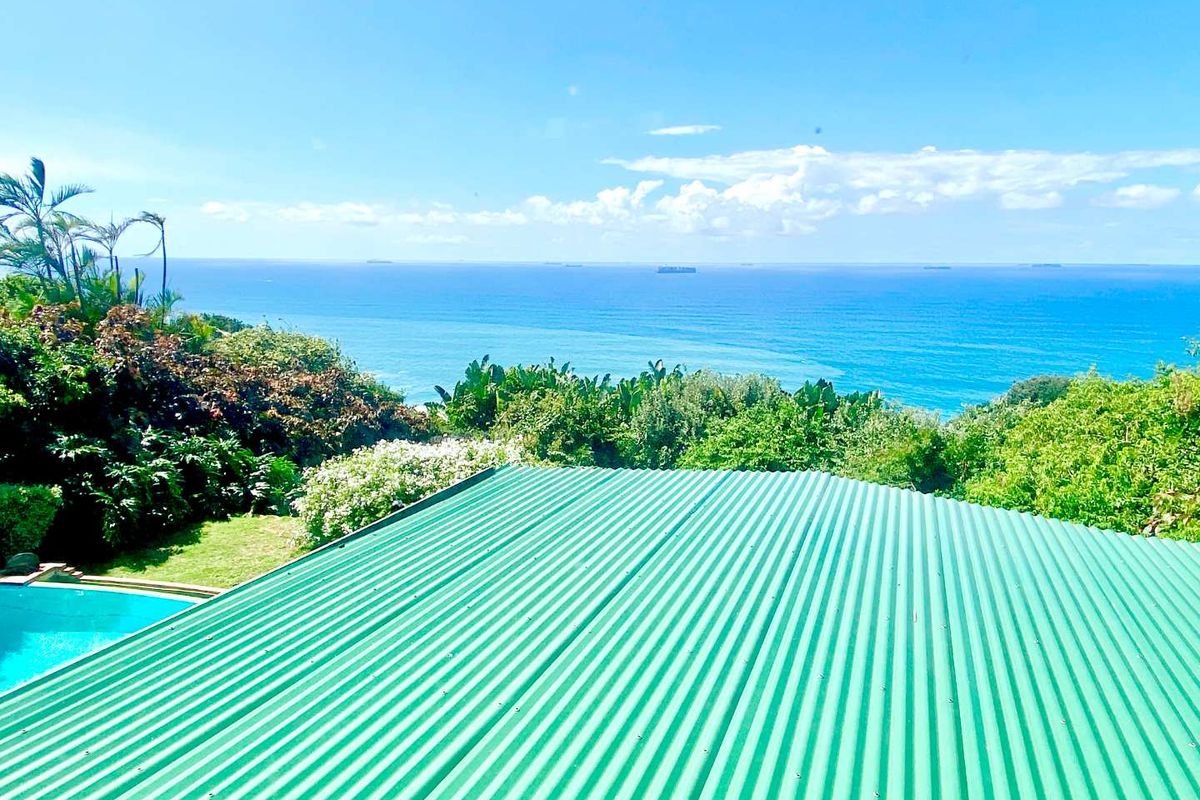 Elevated view overlooking the ocean, featuring a green corrugated metal roof and a glimpse of the swimming pool below.