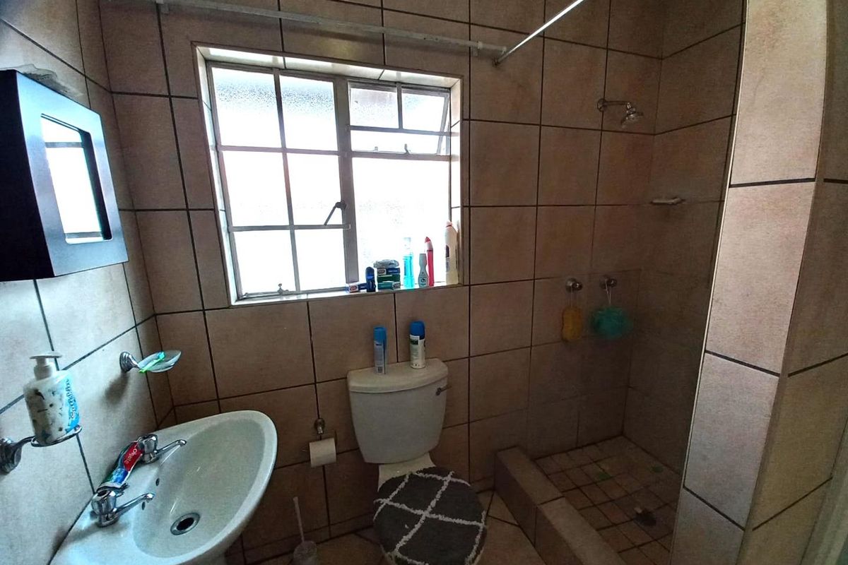 A functional bathroom featuring a pedestal basin, a toilet, and a tiled shower enclosure with a window for natural light.