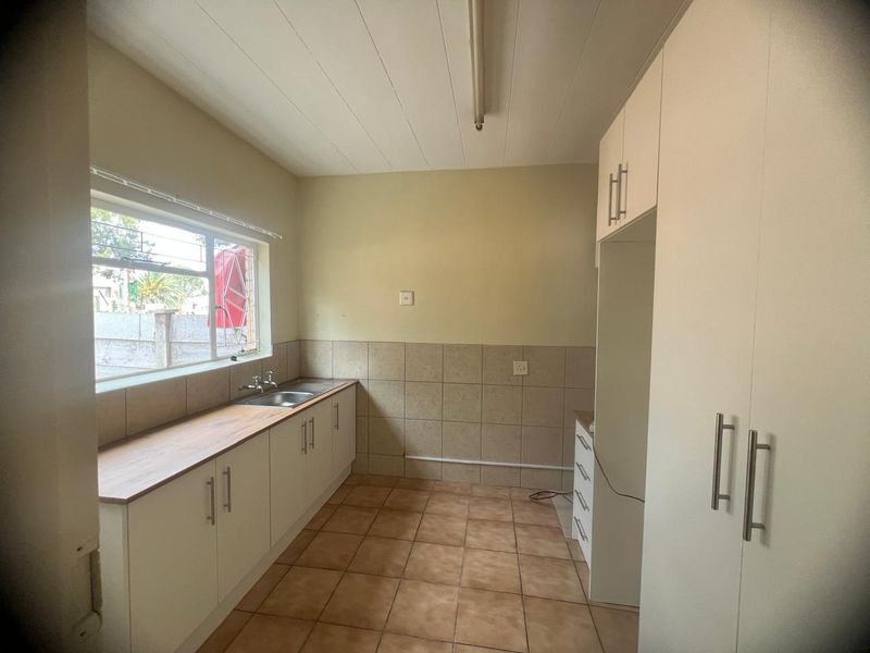 A functional, empty kitchen featuring built-in cabinetry, a stainless steel sink, tiled splashbacks, and tiled flooring, offering a clean canvas for updates.
