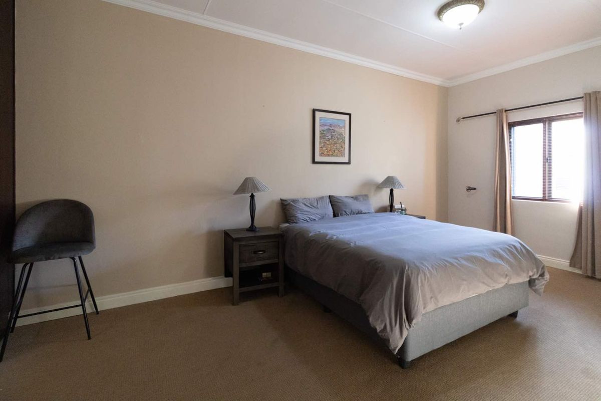 A spacious bedroom featuring neutral wall tones, carpeted flooring, and a window with curtain tracks, providing a comfortable and functional living space.