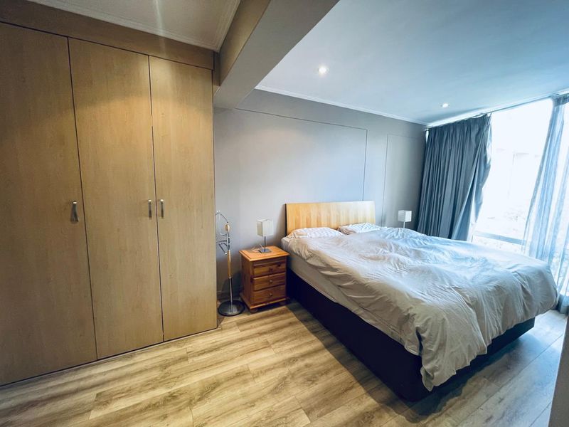 A well-maintained bedroom featuring light wood-tone built-in cupboards, modern laminate flooring, and recessed downlighting, offering a clean and functional living space.