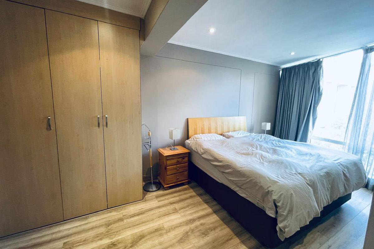 A well-maintained bedroom featuring light wood-tone built-in cupboards, modern laminate flooring, and recessed downlighting, offering a clean and functional living space.