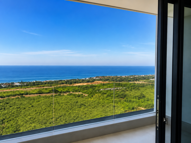 A stunning elevated view of the coastline and ocean, framed by a modern balcony with a sleek glass balustrade.