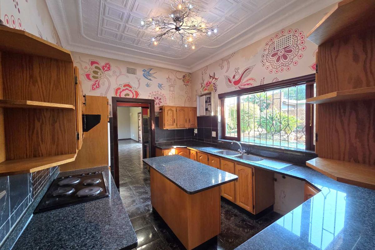Kitchen featuring wooden cabinetry, granite countertops, electric hob, and decorative ceiling tiles, with a view of the garden through the window.