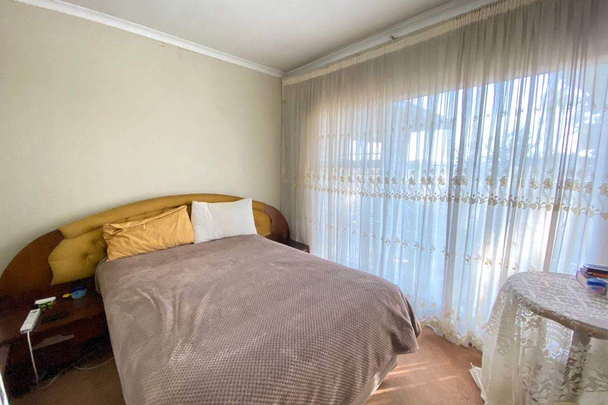 A bedroom featuring a built-in headboard and large window with sheer curtains, providing natural light and a neutral foundation for updates.