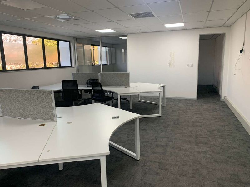 A functional office space featuring carpet tiles, a suspended ceiling with recessed lighting, and a glass partition wall, providing a professional work environment.