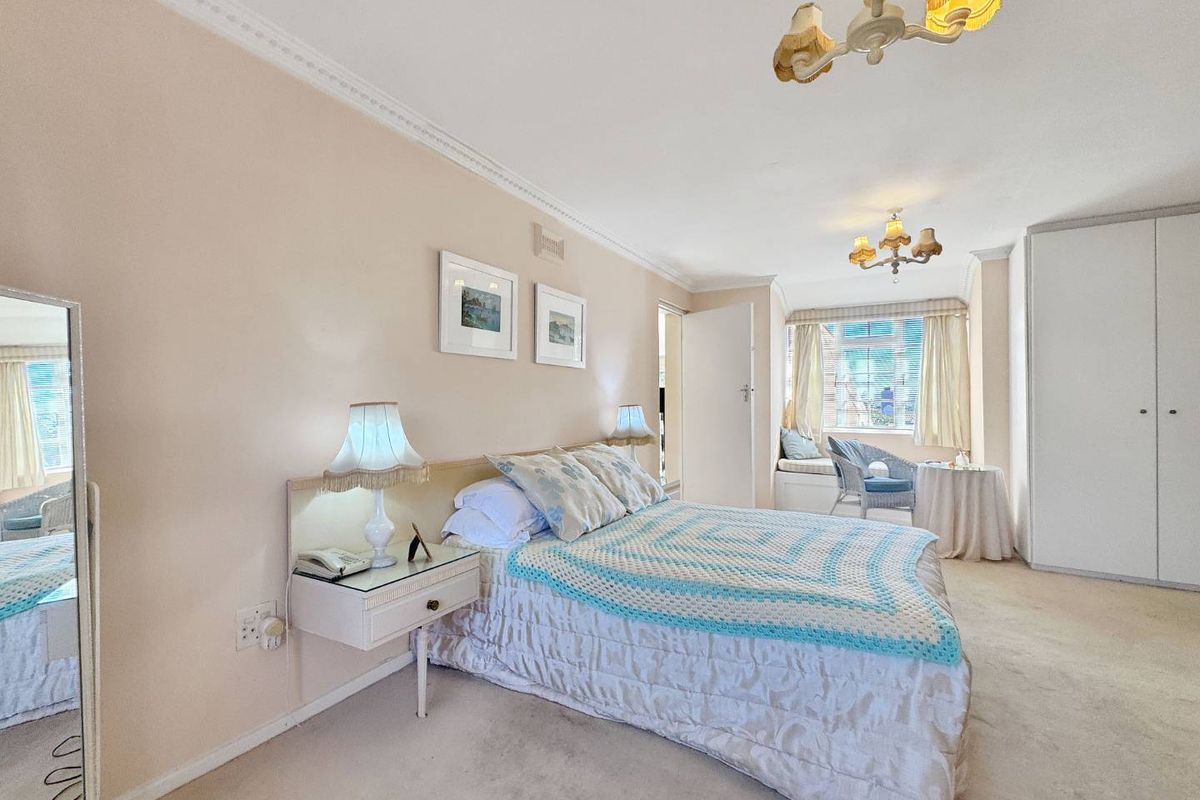 Spacious bedroom featuring built-in wardrobes, crown molding, and a cozy window seat, offering a comfortable and functional living space.