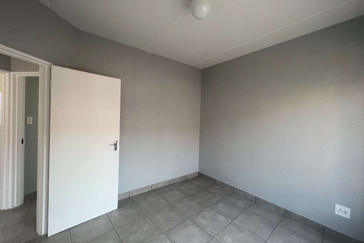 A clean, empty bedroom featuring neutral grey walls, tiled flooring, and a simple overhead light fixture.