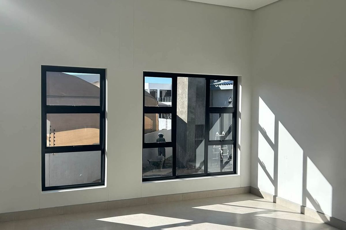 A bright, empty living area featuring neutral tiled flooring and modern black aluminium window frames, offering a clean and versatile space.