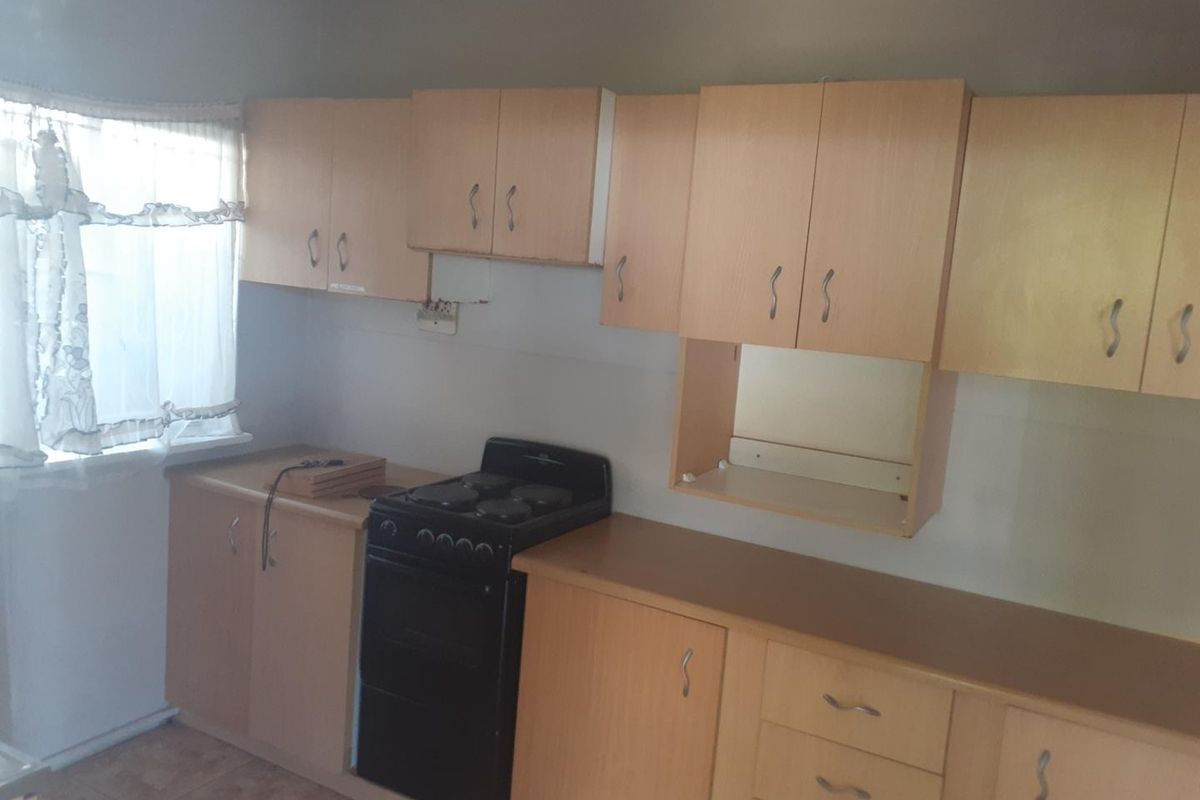 A functional kitchen featuring light wood-look cabinetry, laminate countertops, and a freestanding electric stove, offering a practical layout for daily meal preparation.