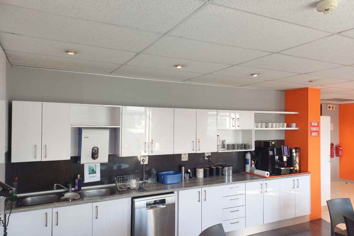 A functional office kitchenette featuring white cabinetry, a stainless steel sink, integrated dishwasher, and a suspended acoustic tile ceiling with recessed lighting.