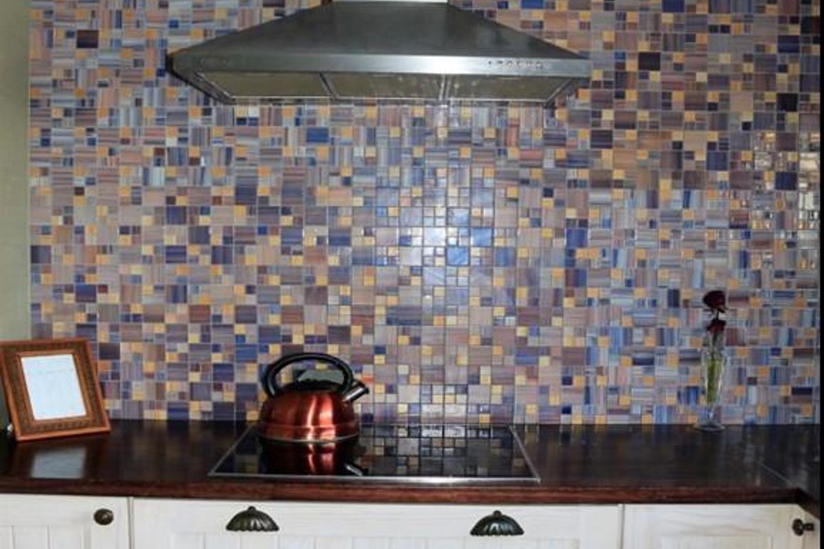A kitchen area featuring a decorative mosaic tile backsplash, stainless steel extractor fan, electric cooktop, and wooden countertops with built-in cabinetry.
