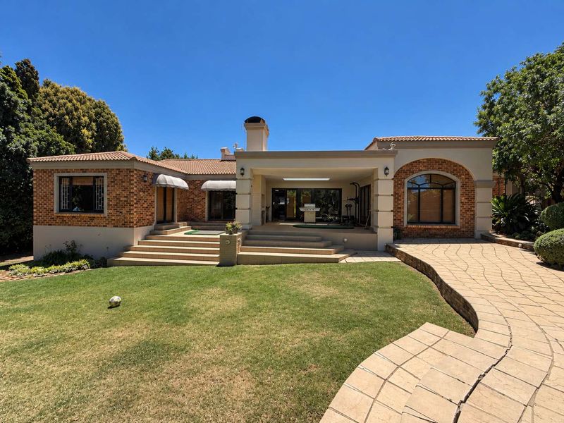 Rear view of a well-maintained brick house featuring a covered patio, stone paved walkway, and landscaped garden area.