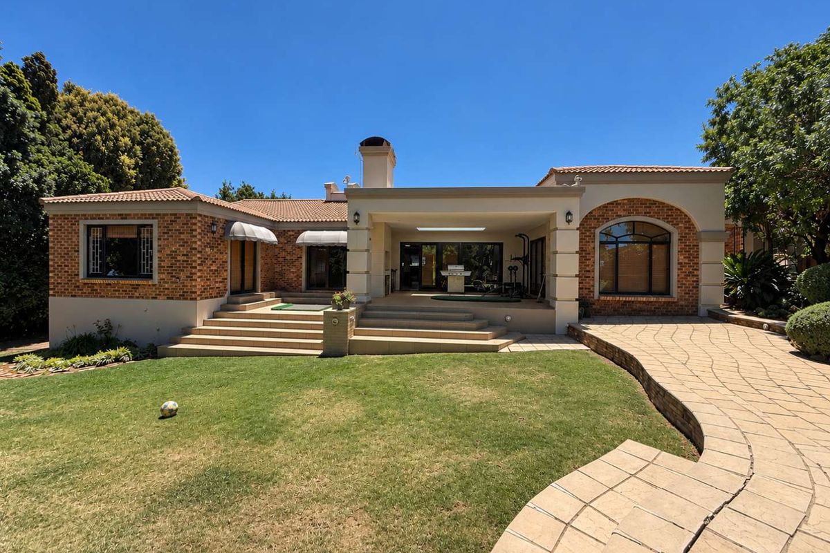 Rear view of a well-maintained brick house featuring a covered patio, stone paved walkway, and landscaped garden area.