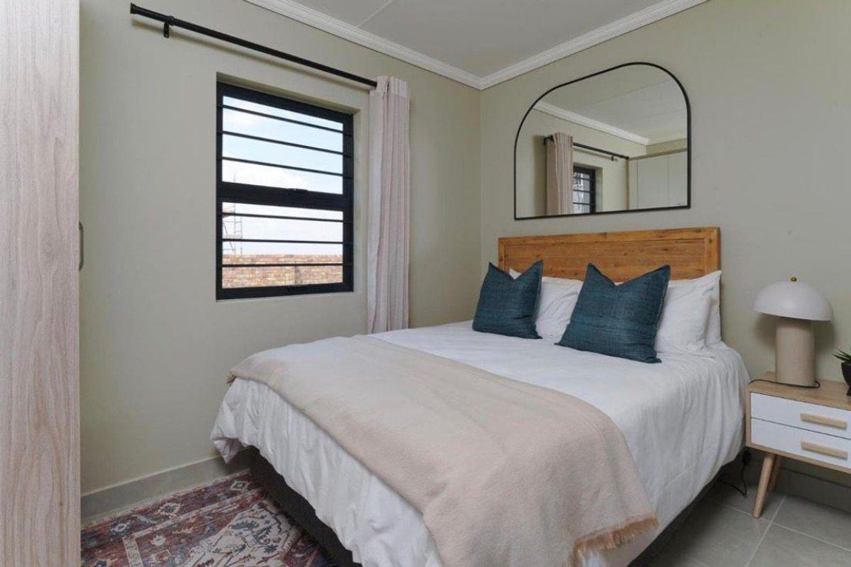 A well-maintained bedroom featuring neutral wall tones, tiled flooring, and a window with security bars, providing a clean and functional living space.