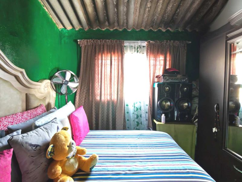 A bedroom featuring a corrugated iron ceiling and a window with security bars.