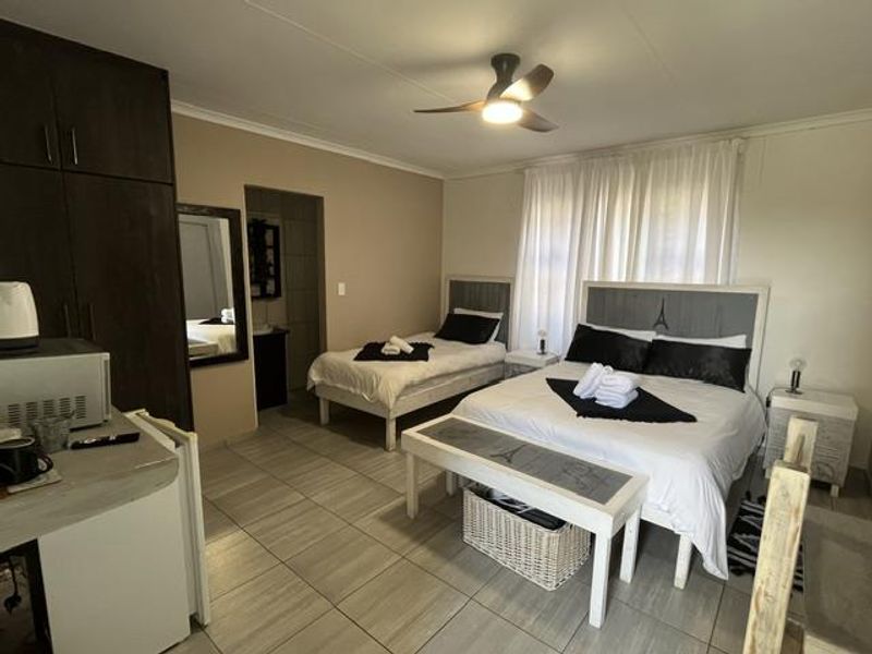 A well-maintained bedroom featuring tiled flooring, built-in cupboards, and a ceiling fan, with an adjoining en-suite bathroom area.